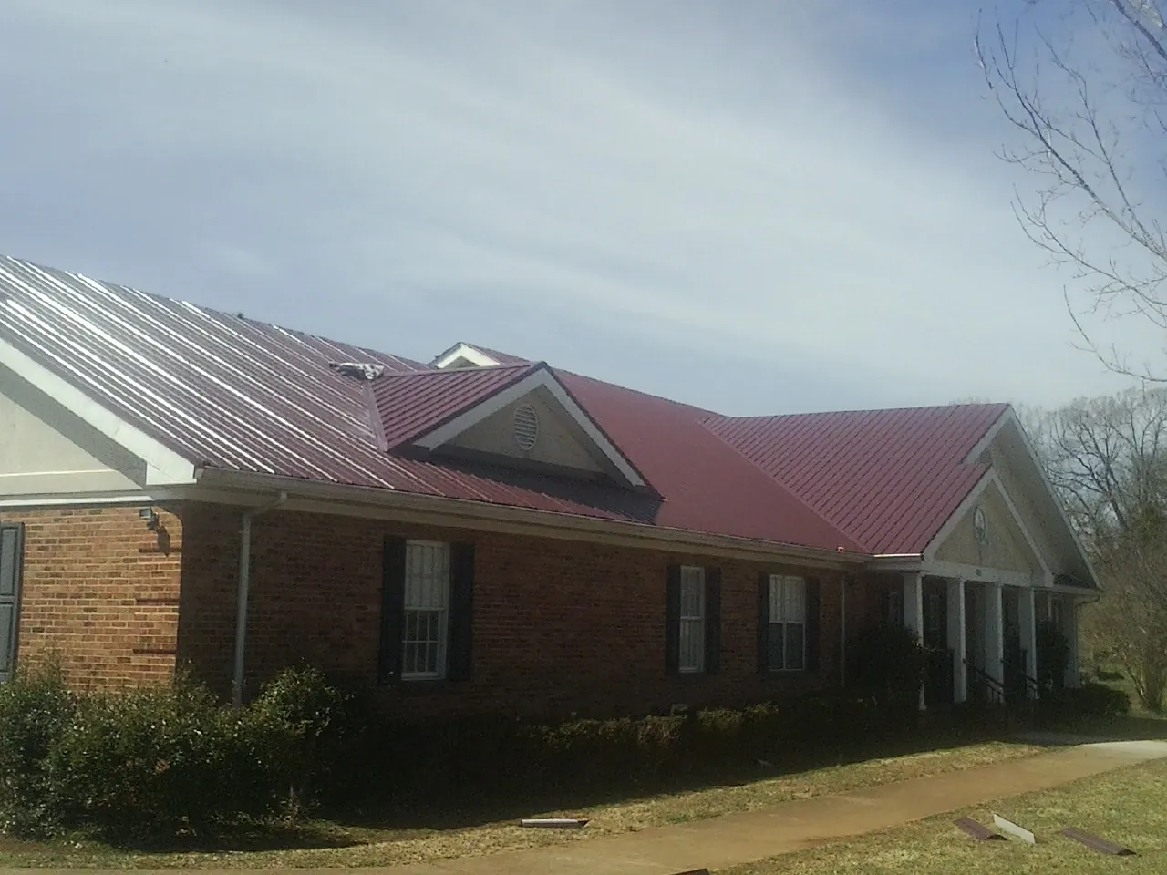 Red metal roof with gabled entries on a long brick building, from a Hail Damage Roof Repair job in Nisswa