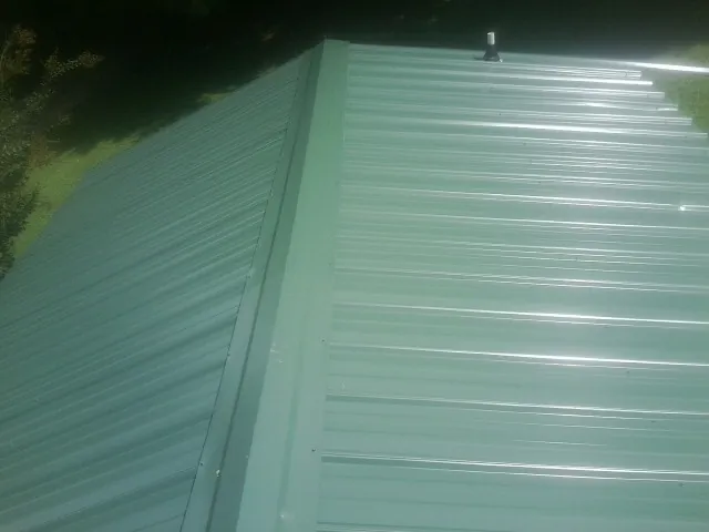 New green metal panels meeting at the ridge of a roof — Flat Roof Repair work by our crew in Nisswa
