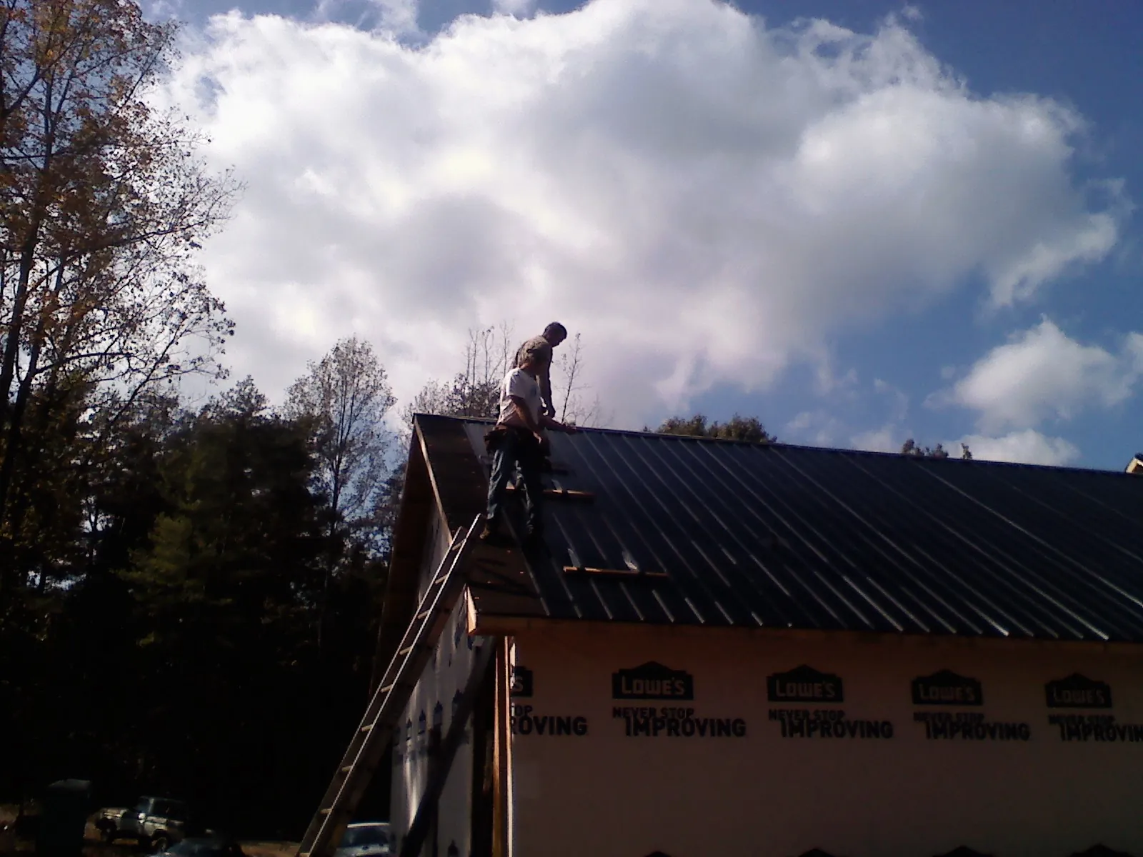 Roofer fastening dark metal panels high against a cloudy sky, from a Roof Inspection job in Nisswa