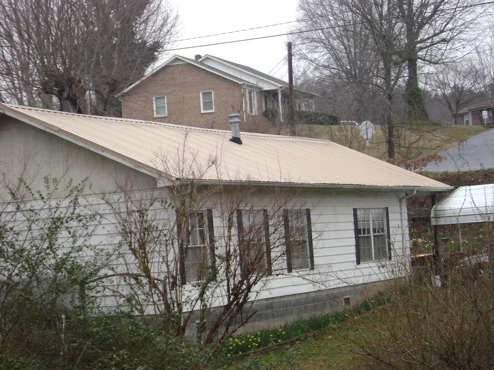 Tan metal roof on a white sided house set into a hillside — Commercial Roofing by Roofing Brothers in Nisswa