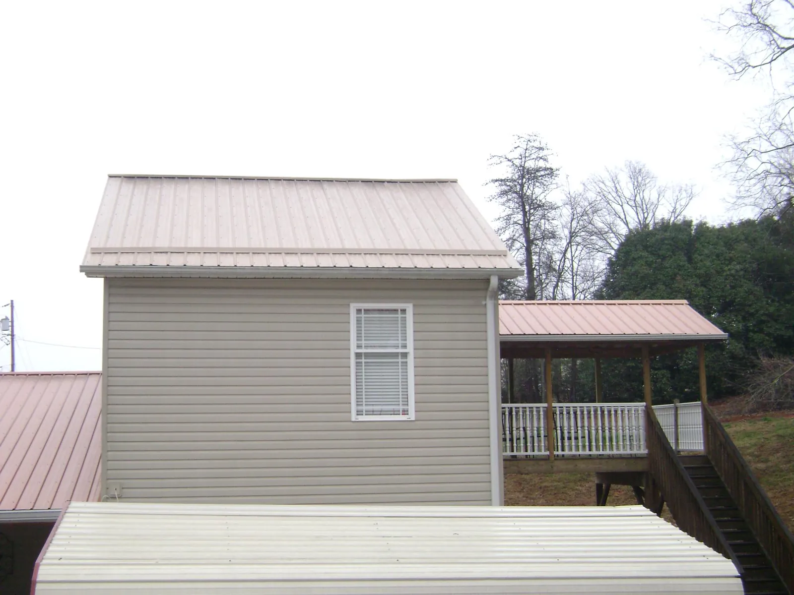 Tan metal roofs on a two story addition and attached porch, from a Roof Replacement job in Nisswa